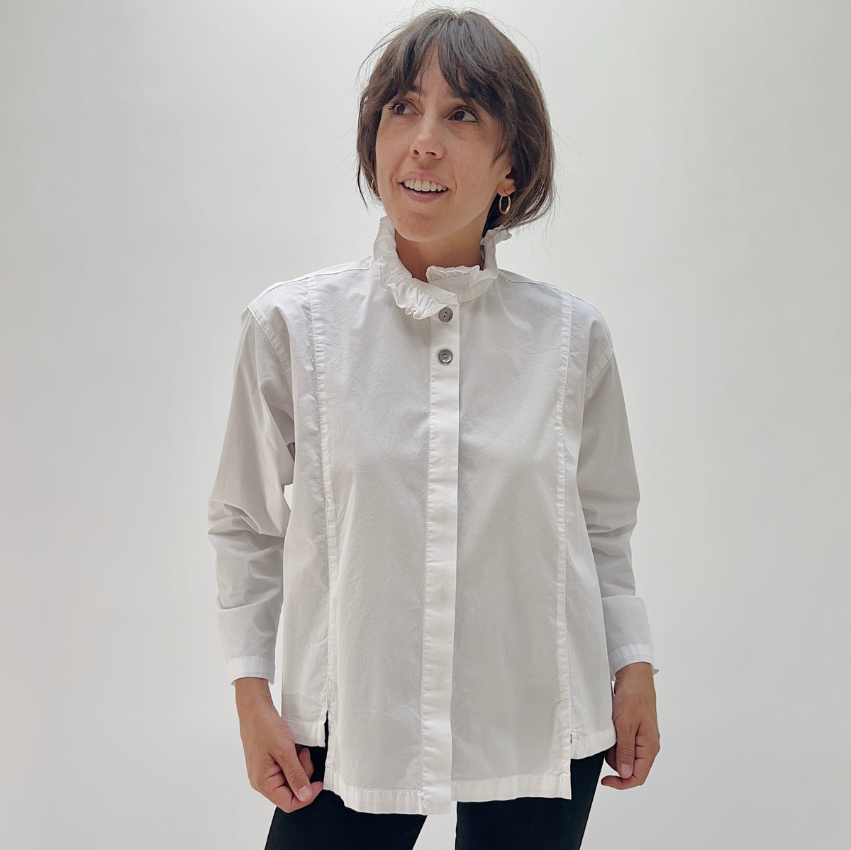 Model wearing the Eleven Stitch Tuxedo Shirt in Chalk, front view, relaxed white cotton button-down with ruffled stand collar and shell buttons, styled with black pants
