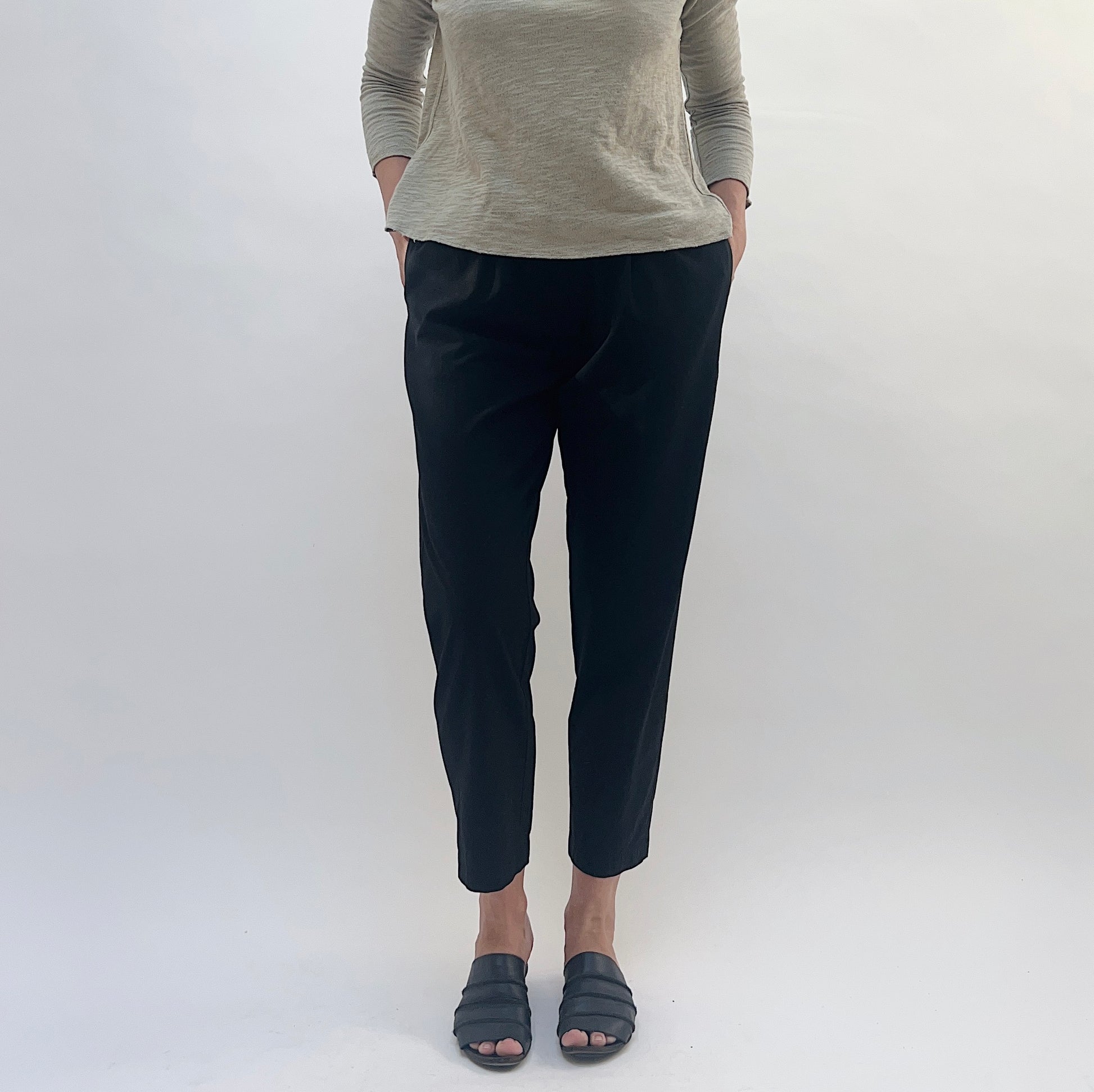 Person wearing black pants and a gray top against a white background