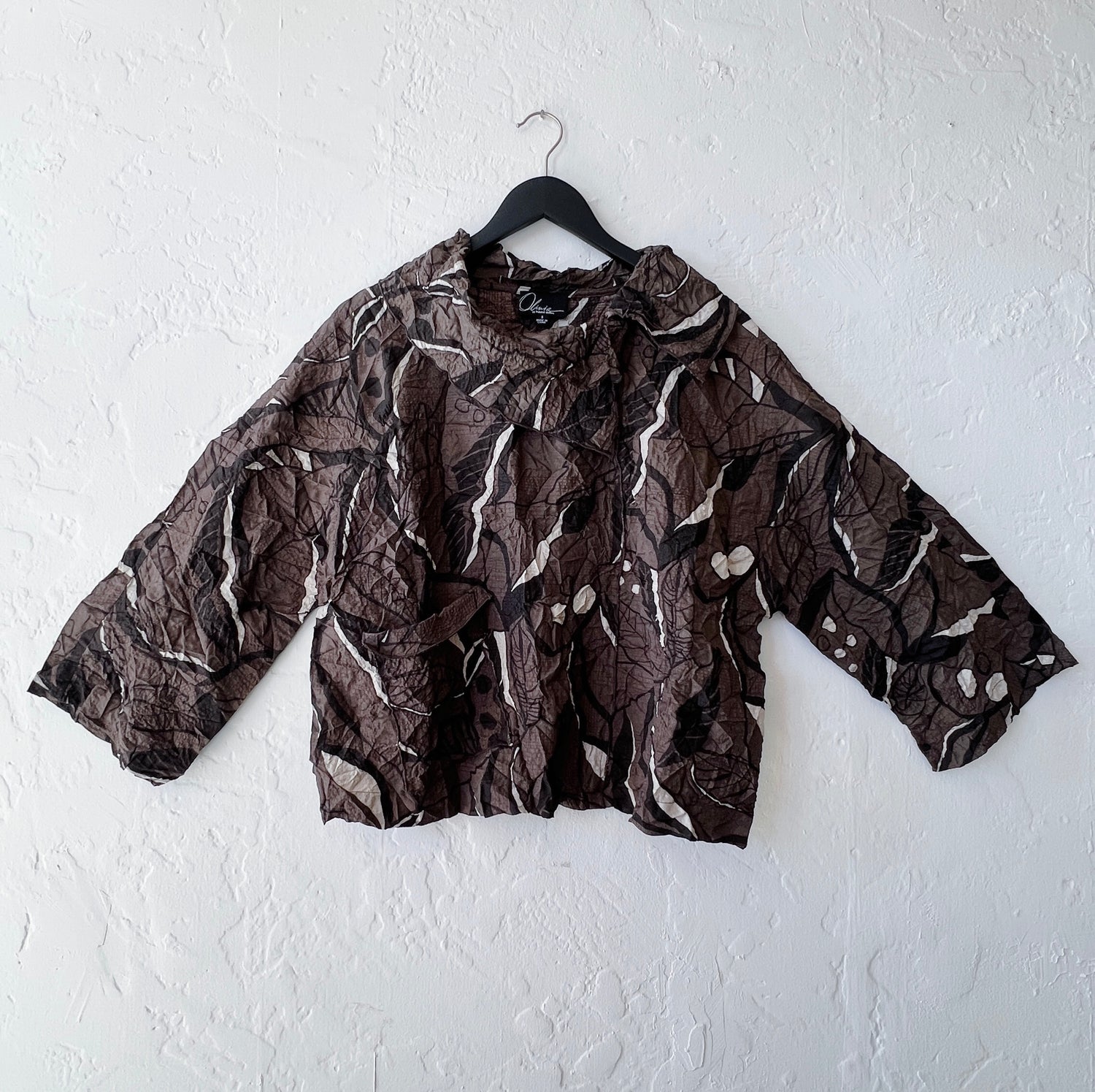 Brown leaf patterned shirt on a hanger against a white wall
