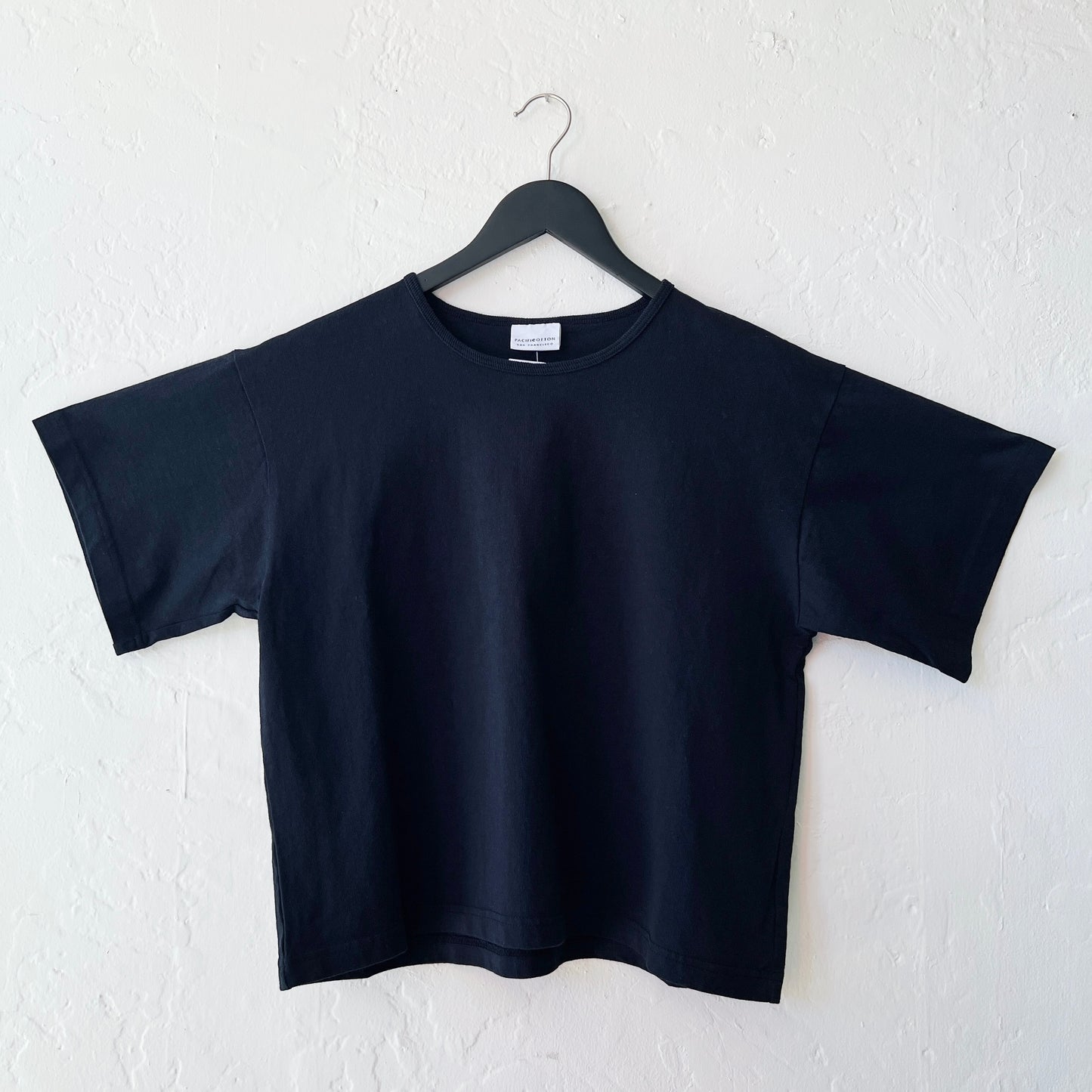 Black t-shirt on a hanger against a white wall