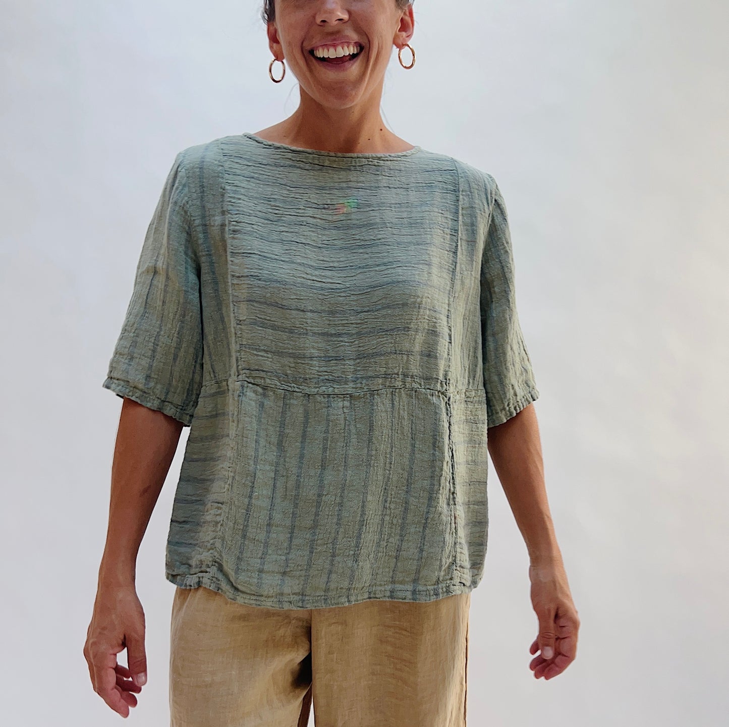 Model wearing the Seamed Boxy Striped Top in Balsam Green, a relaxed short-sleeve top with a textured stripe pattern, seamed waist detail, and crew neck, styled with tan linen pants