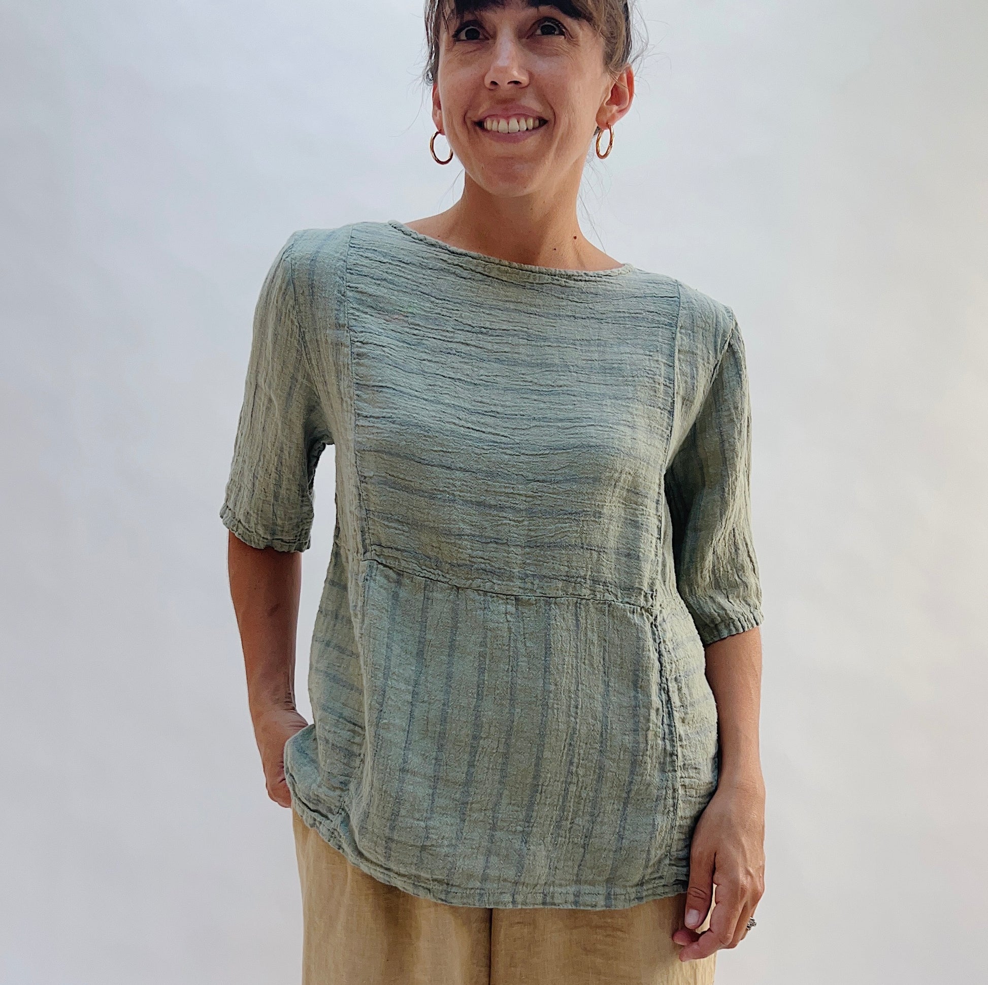 Model wearing the Seamed Boxy Striped Top in Balsam Green, a relaxed short-sleeve top with a textured stripe pattern, seamed waist detail, and crew neck, styled with tan linen pants
