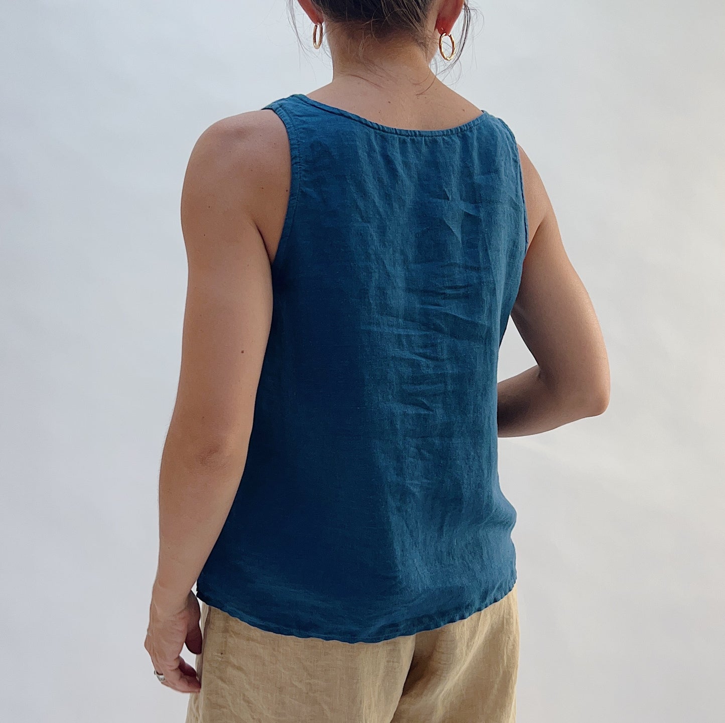 Back view of the Basic Tank in French Navy by Yuvita, showing the relaxed linen drape, wide straps, and scoop back in deep teal blue, styled with tan linen trousers