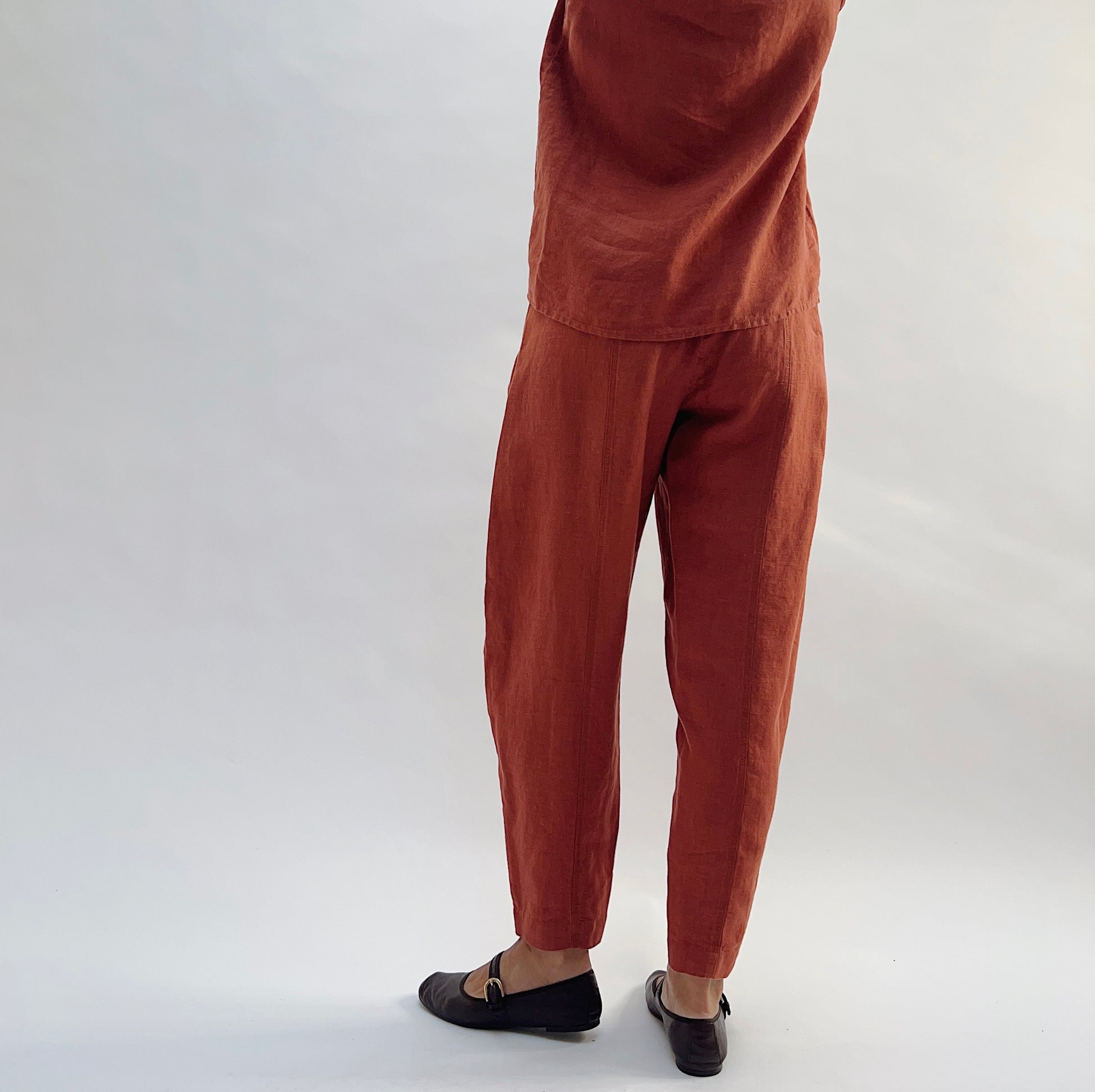Back view of the Seamed Taper Pant in Terracotta by Yuvita, showing the clean linen back, elastic waistband, and tapered ankle, styled with a matching terracotta linen top and dark Mary Jane flats