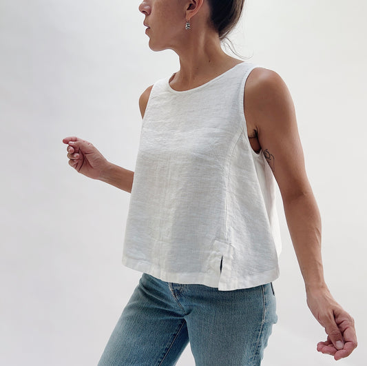 Side three-quarter view of the Button Back Tank in White by Yuvita, showing the relaxed linen drape, side slit, and cropped hem, styled with blue jeans