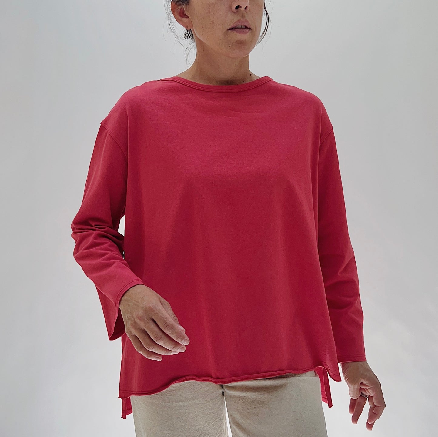 North Star Base Cotton Jersey Beach Tee in Cayenne — front view showing the oversized boxy fit, crew neckline, long sleeves, and curved hem with side slits in cayenne red, worn with cream trousers on a white background