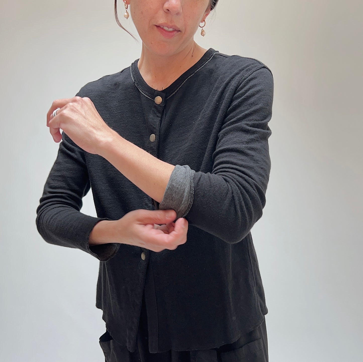 Model rolling the sleeve cuff on the black cardigan, highlighting contrast lining and snap placket detail