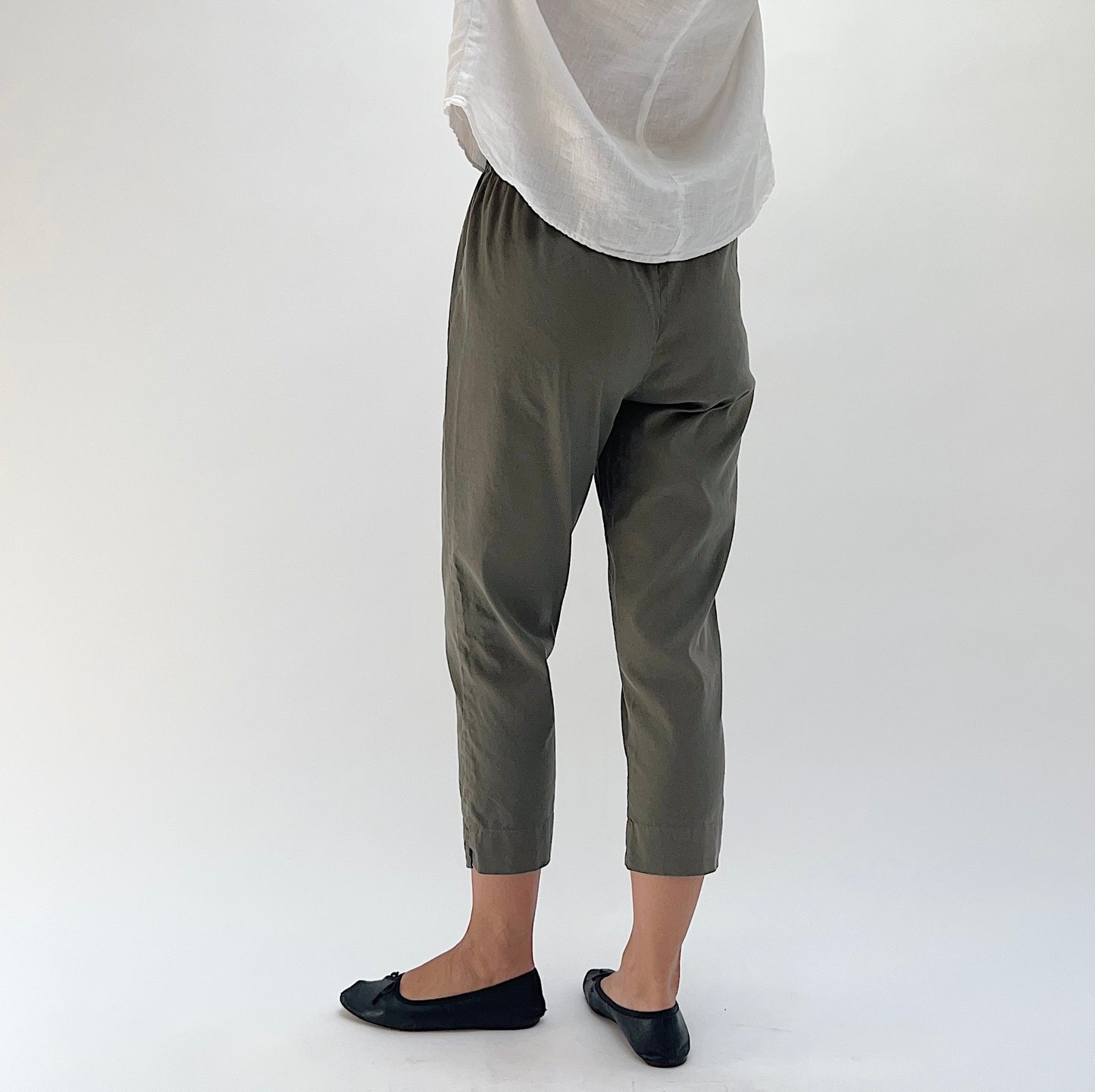 Back view of model wearing Cut Loose linen-Tencel crop pant in kelp, showing tapered silhouette, side seam vent at hem, and elastic waistband