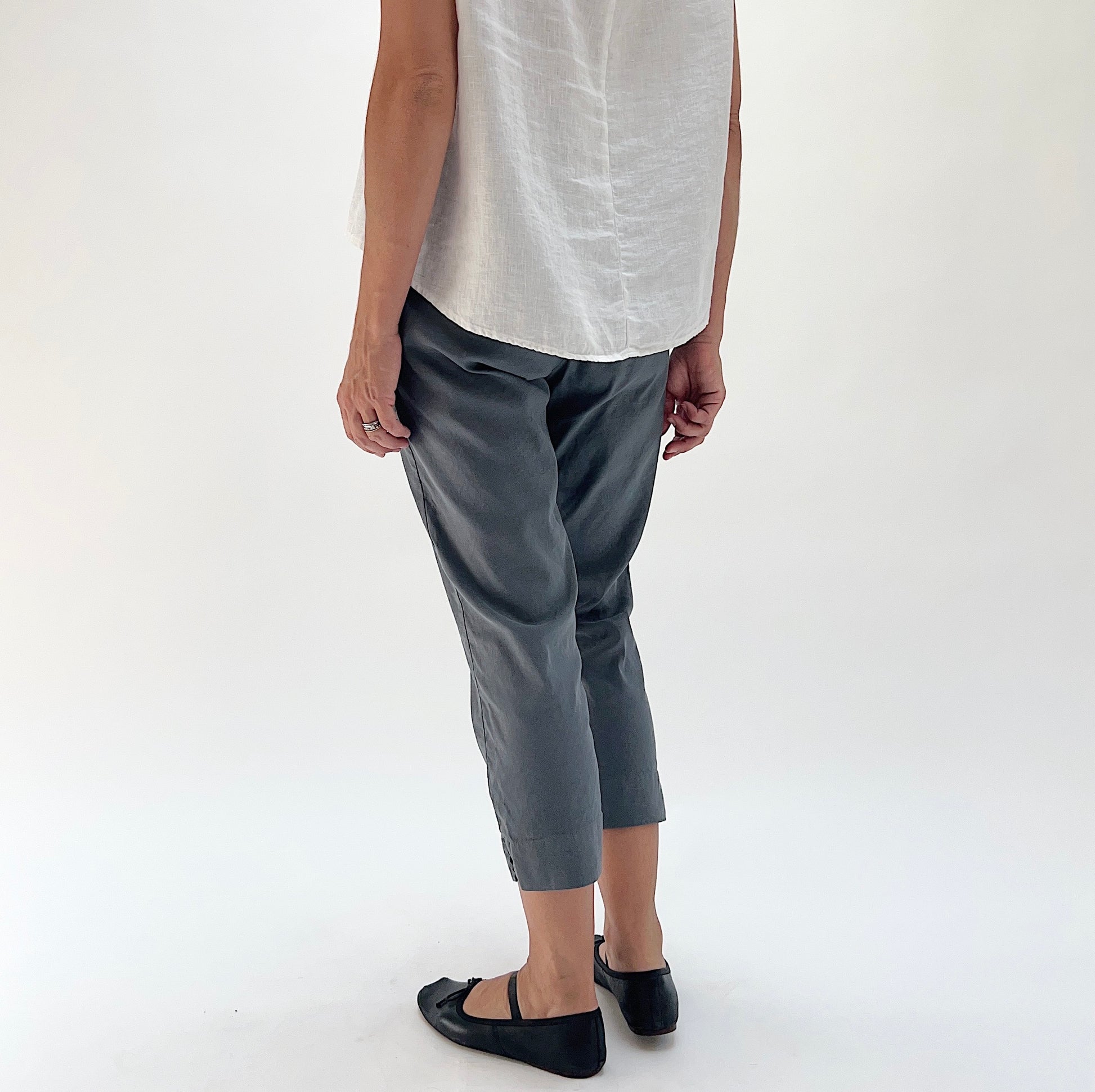 Back three-quarter view of model wearing Cut Loose iron grey taper crop pant, showing relaxed hip fit, tapered silhouette, and side seam vent at hem