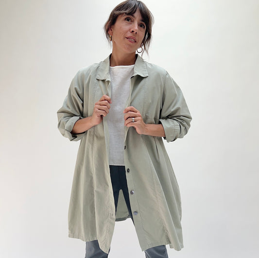 Model holding open Eleven Stitch artichoke darted coat, showing button-front closure, point collar, and relaxed A-line silhouette layered over a white tee