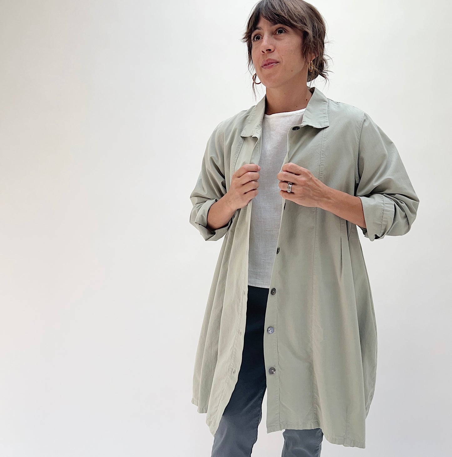 Full front view of model wearing Eleven Stitch artichoke darted coat open, showing knee length, front patch pockets, and darted shaping at the waist
