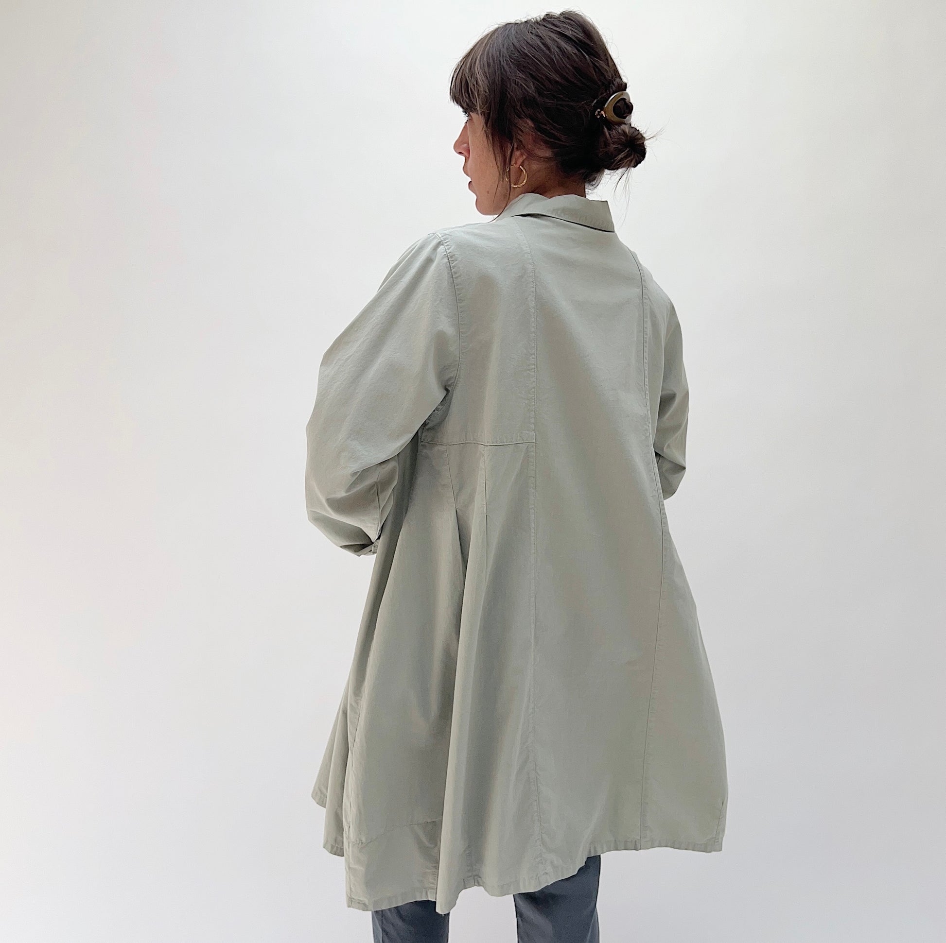 Back view of model wearing Eleven Stitch artichoke darted coat, showing back dart detailing, A-line flare, and knee-length hem