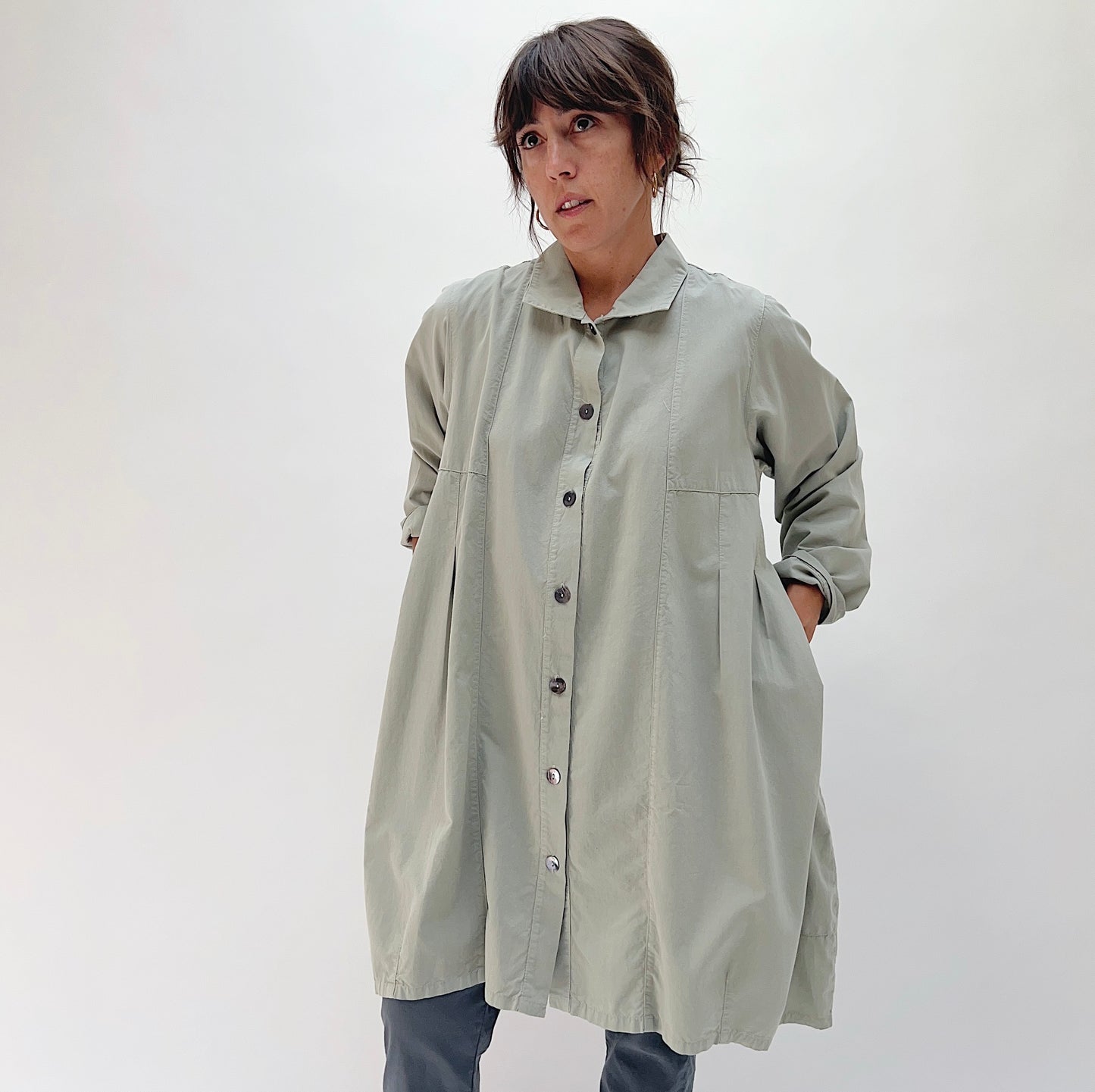 Front view of model wearing Eleven Stitch artichoke darted coat buttoned closed, showing point collar, button placket, front patch pockets, and full coat length