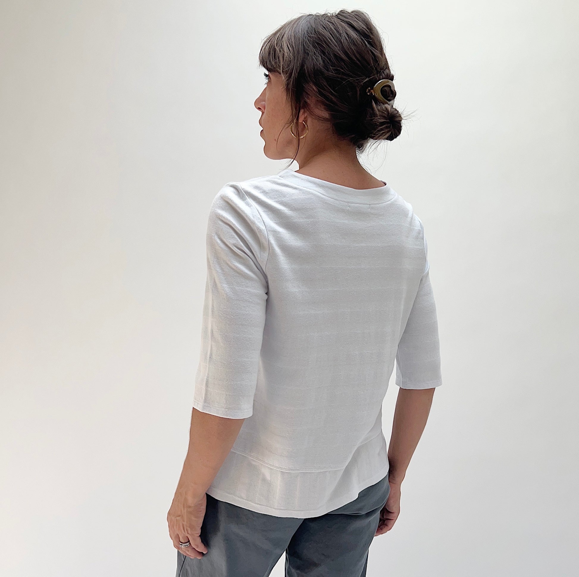 Back view of model wearing Habitat white shadow stripe elbow sleeve top, showing relaxed fit, elbow-length sleeves, and curved layered hem