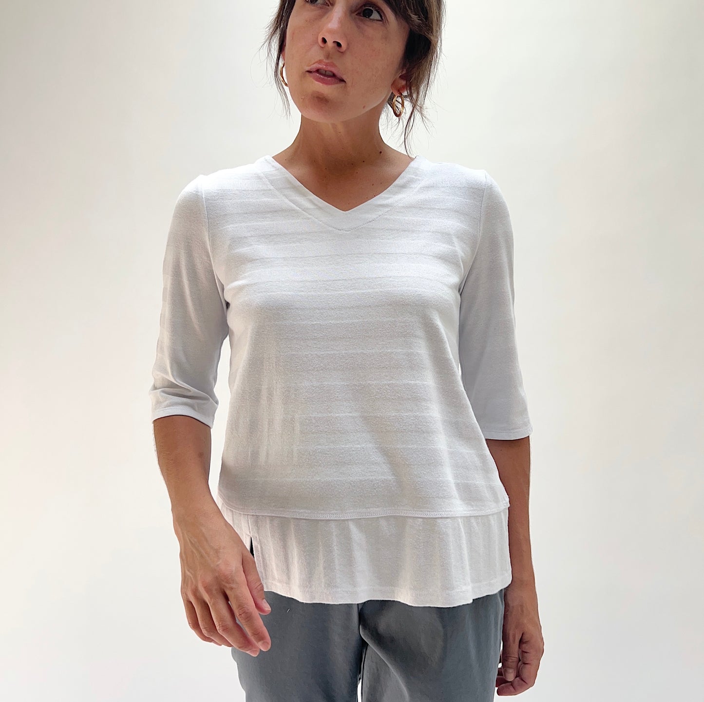 Three-quarter front view of model wearing Habitat white shadow stripe top, showing V-neckline, tonal horizontal stripe texture, and layered hem detail