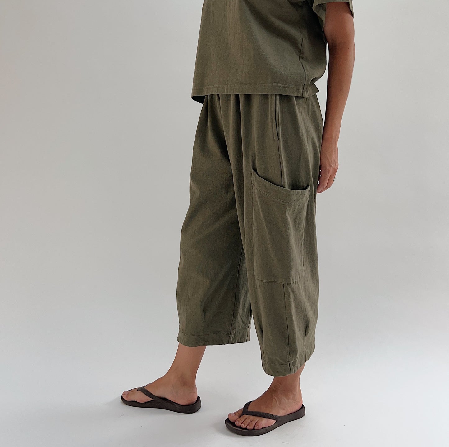 Side view of model wearing Bryn Walker jasper Pasha pant, showing large patch pocket detail, wide-leg drape, and banded hem at ankle