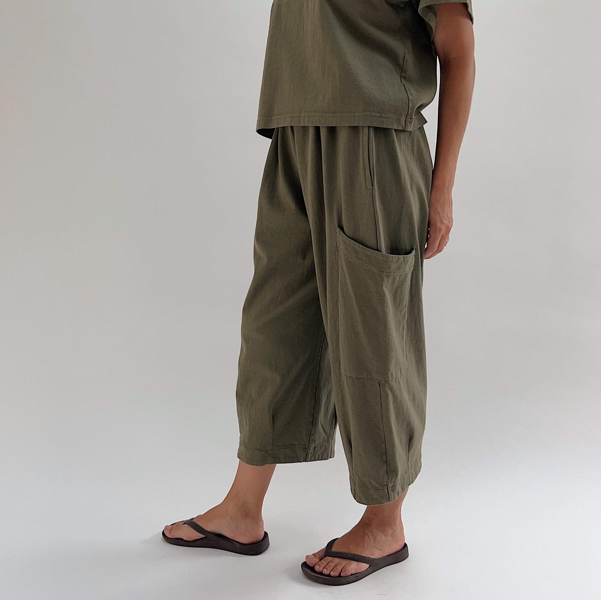 Side view of model wearing Bryn Walker jasper Pasha pant, showing large patch pocket detail, wide-leg drape, and banded hem at ankle