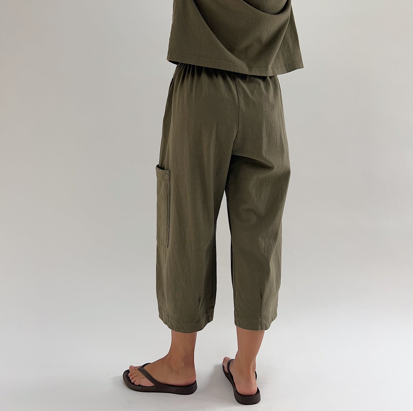 Back three-quarter view of model wearing Bryn Walker jasper cotton Pasha pant, showing elastic waistband, patch pocket on back leg, and cropped wide-leg silhouette