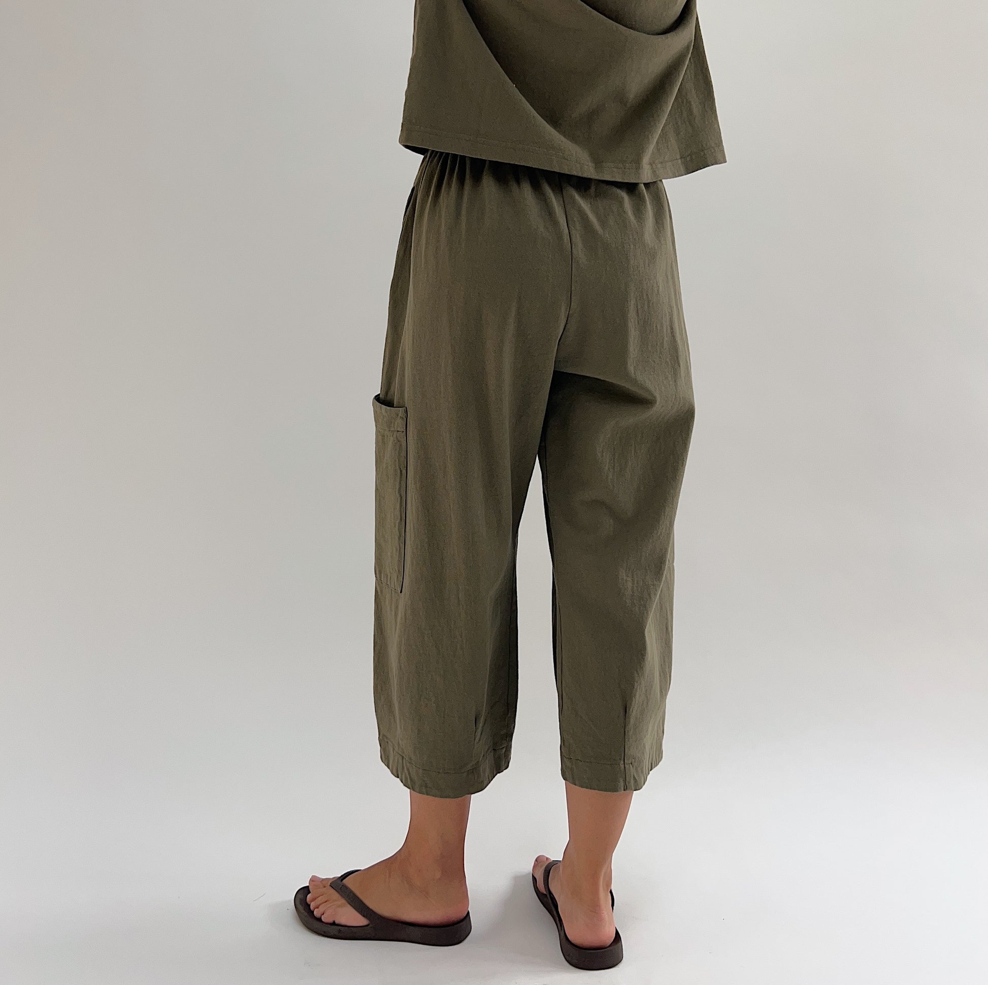 Back three-quarter view of model wearing Bryn Walker jasper cotton Pasha pant, showing elastic waistband, patch pocket on back leg, and cropped wide-leg silhouette