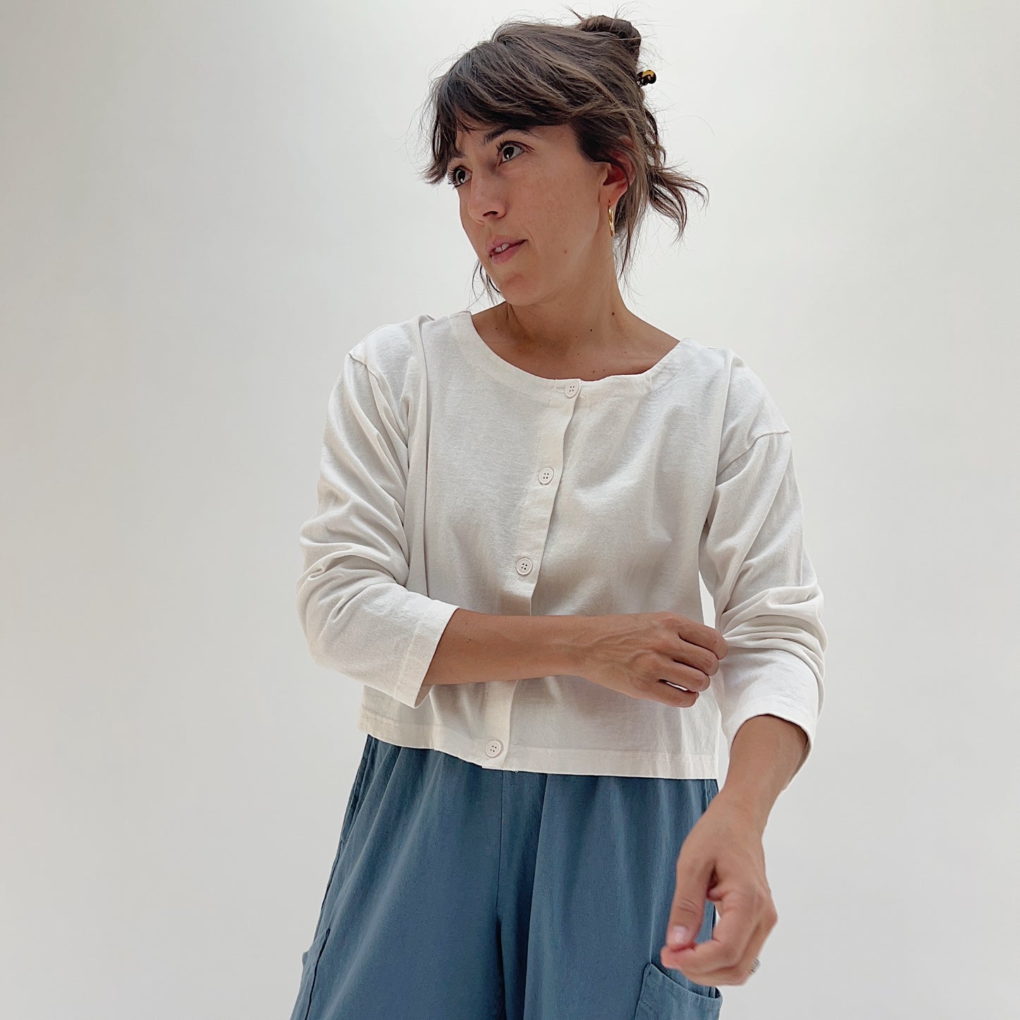 Three-quarter front view of model wearing Pacific Cotton cream long sleeve button-front shirt, showing crew neckline, center button placket, and relaxed cropped fit