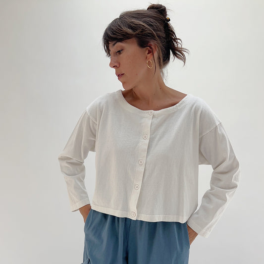Full front view of model wearing Pacific Cotton cream button-front shirt, showing crew neckline, four-button placket, long sleeves, and straight cropped hem
