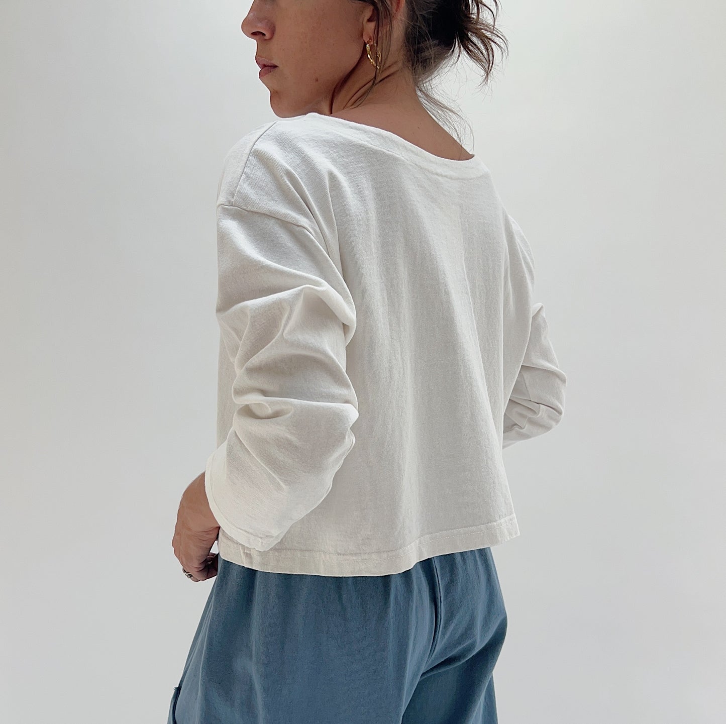 Back view of model wearing Pacific Cotton cream long sleeve button-front shirt, showing relaxed boxy silhouette, long sleeves, and straight cropped hem