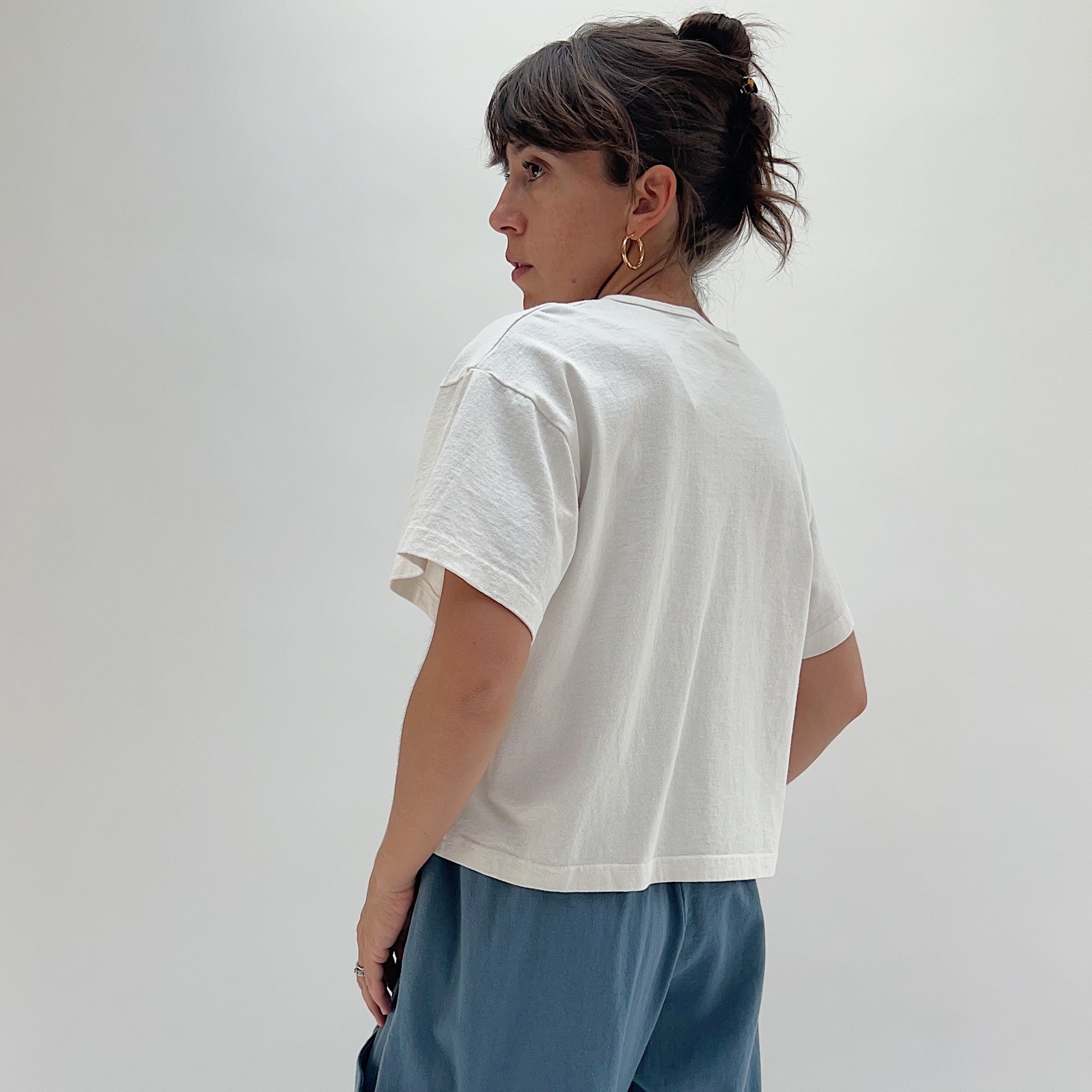 Back three-quarter view of model wearing Pacific Cotton cream crop crew tee, showing boxy silhouette, short sleeves, and straight cropped hem