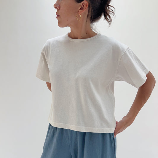 Three-quarter front view of model wearing Pacific Cotton cream crop crew tee, showing crew neckline, relaxed boxy fit, short sleeves, and straight cropped hem