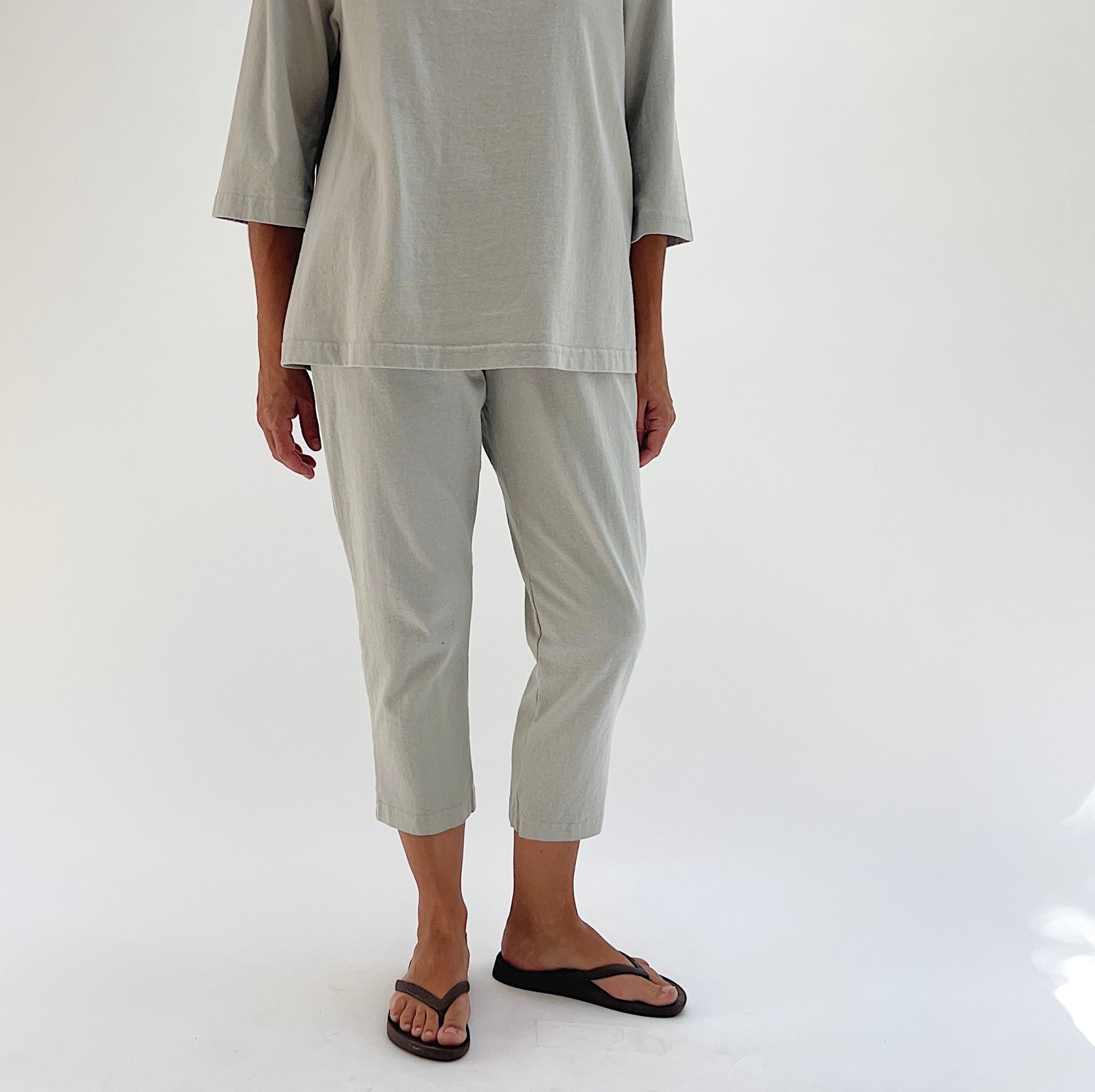 Front view of model wearing Pacific Cotton orlaya Sunday pant, showing elastic waistband, side pocket, cropped tapered leg, and sage green color