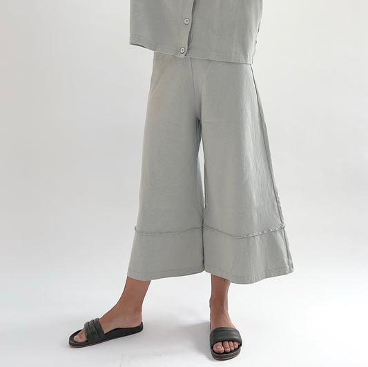 Three-quarter front view of model wearing Pacific Cotton orlaya crop full pant, showing elastic waistband, wide flared leg silhouette, layered hem panel, and cropped length