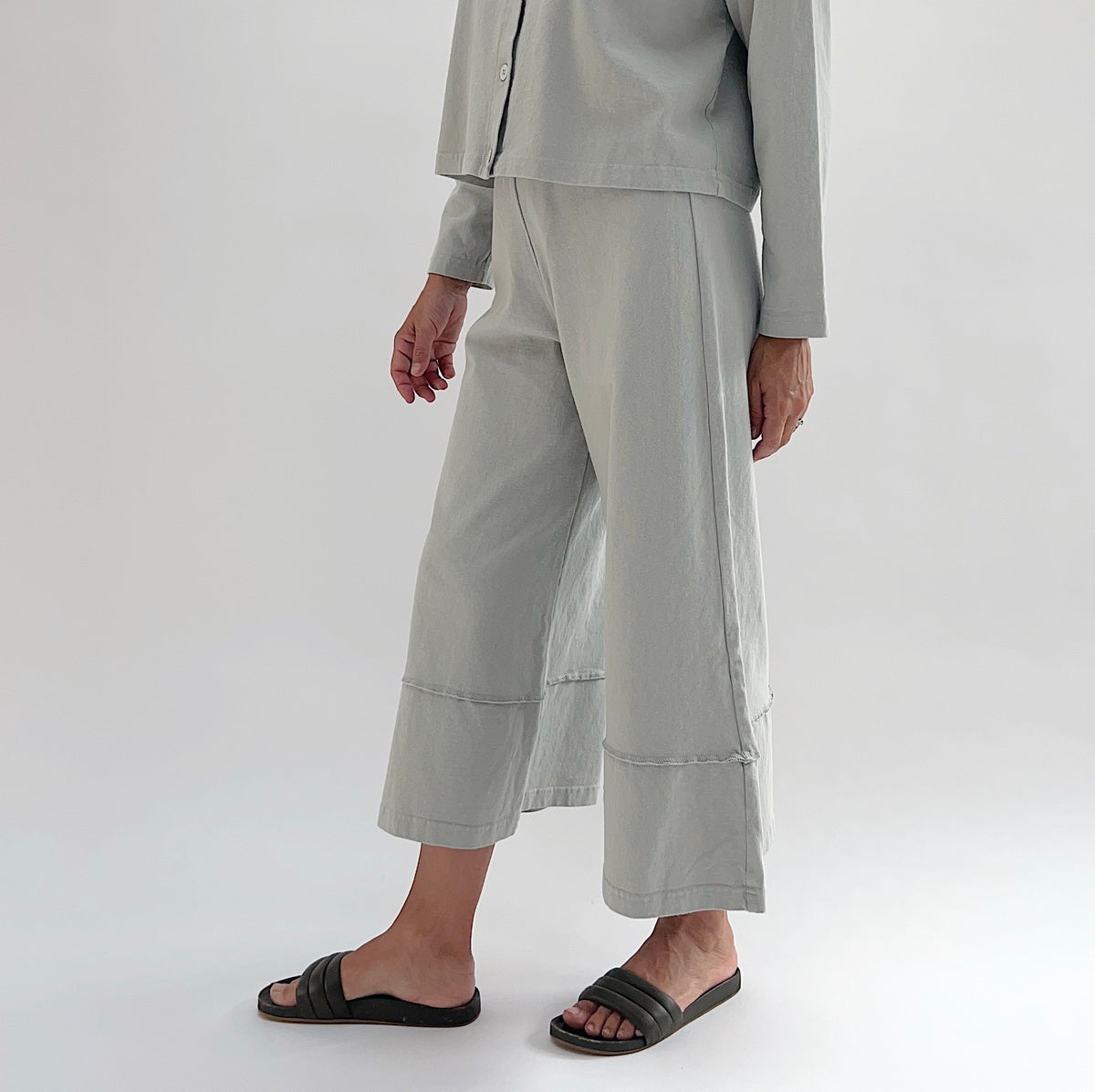 Three-quarter front view of model wearing Pacific Cotton orlaya crop full pant, showing elastic waistband, wide flared leg silhouette, layered hem panel, and cropped length