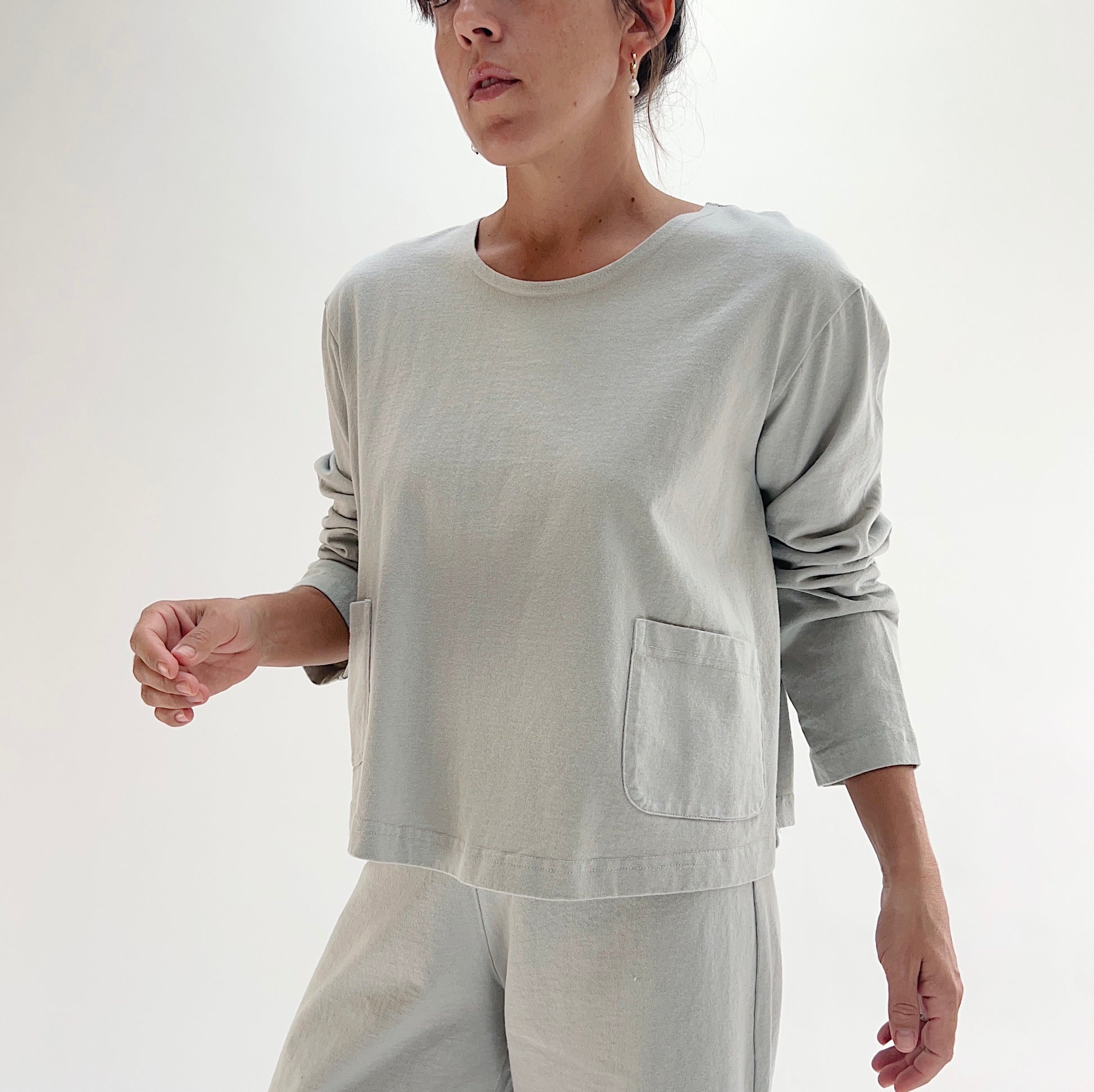 Three-quarter front view of model wearing Pacific Cotton orlaya boxy shirt, showing crew neckline, front patch pocket, long sleeves, boxy cropped silhouette, and banded hem