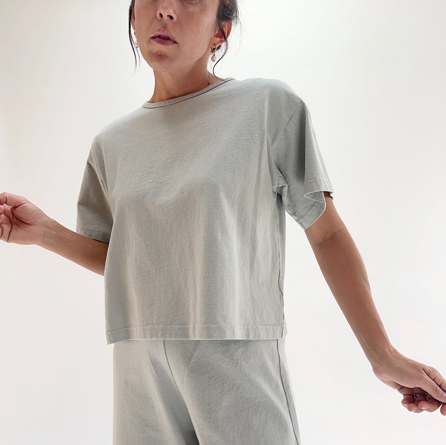 Full front view of model wearing Pacific Cotton orlaya crop crew tee, showing crew neckline, short sleeves, boxy cropped silhouette, banded hem, and sage green color