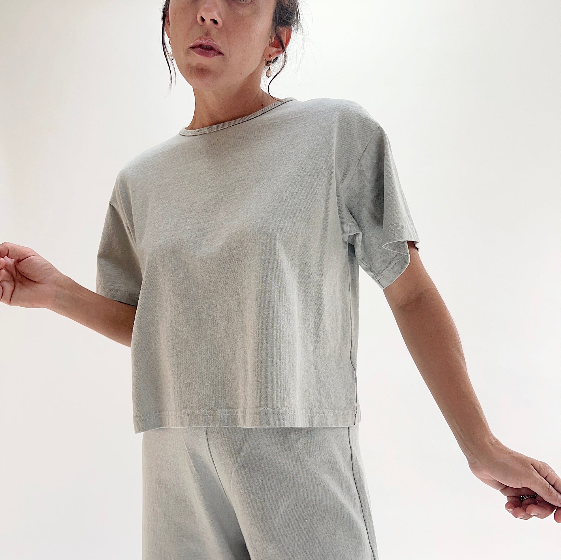 Full front view of model wearing Pacific Cotton orlaya crop crew tee, showing crew neckline, short sleeves, boxy cropped silhouette, banded hem, and sage green color