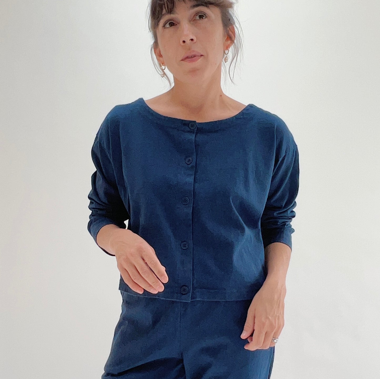 Close front view of model wearing Pacific Cotton nova long sleeve button front shirt, showing wide scoop neckline, five-button center placket, long sleeves, boxy cropped fit, and deep teal color