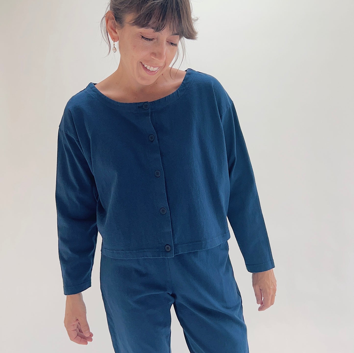 Three-quarter front view of model wearing Pacific Cotton nova long sleeve button front shirt, showing wide scoop neckline, five-button center placket, boxy cropped silhouette, banded hem, and deep teal color
