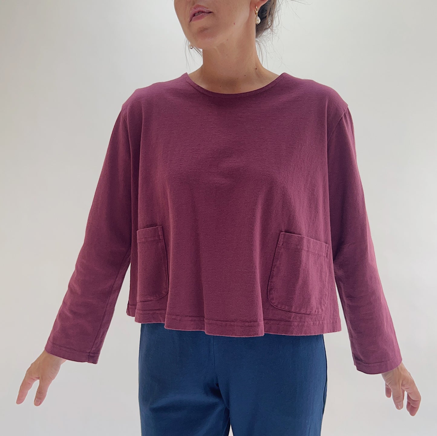Three-quarter front view of model wearing Pacific Cotton rhone boxy shirt, showing crew neckline, front patch pocket, long sleeves, boxy cropped silhouette, and berry plum color