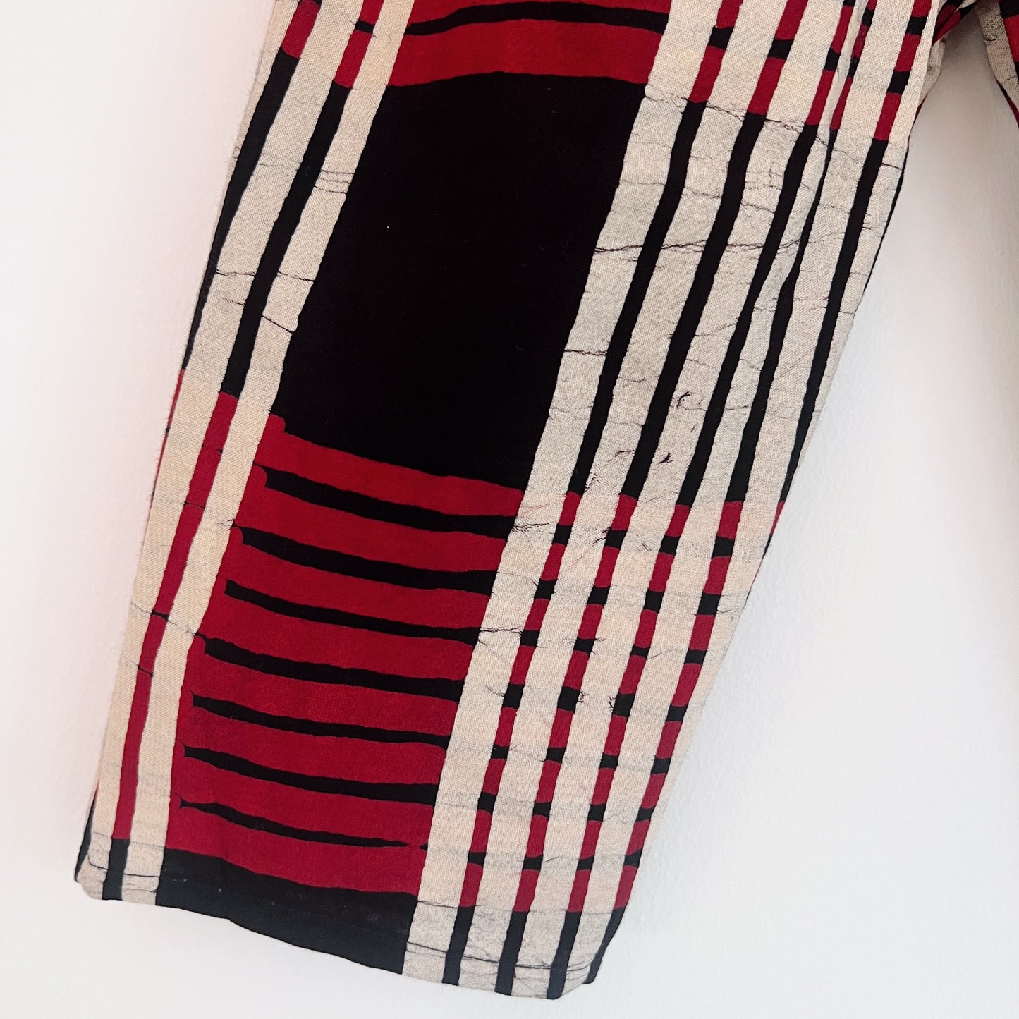 Close-up of hand-printed red plaid Batiki cotton fabric, showing bold red, black, and cream stripe pattern with hand-dyed texture and natural cotton weave