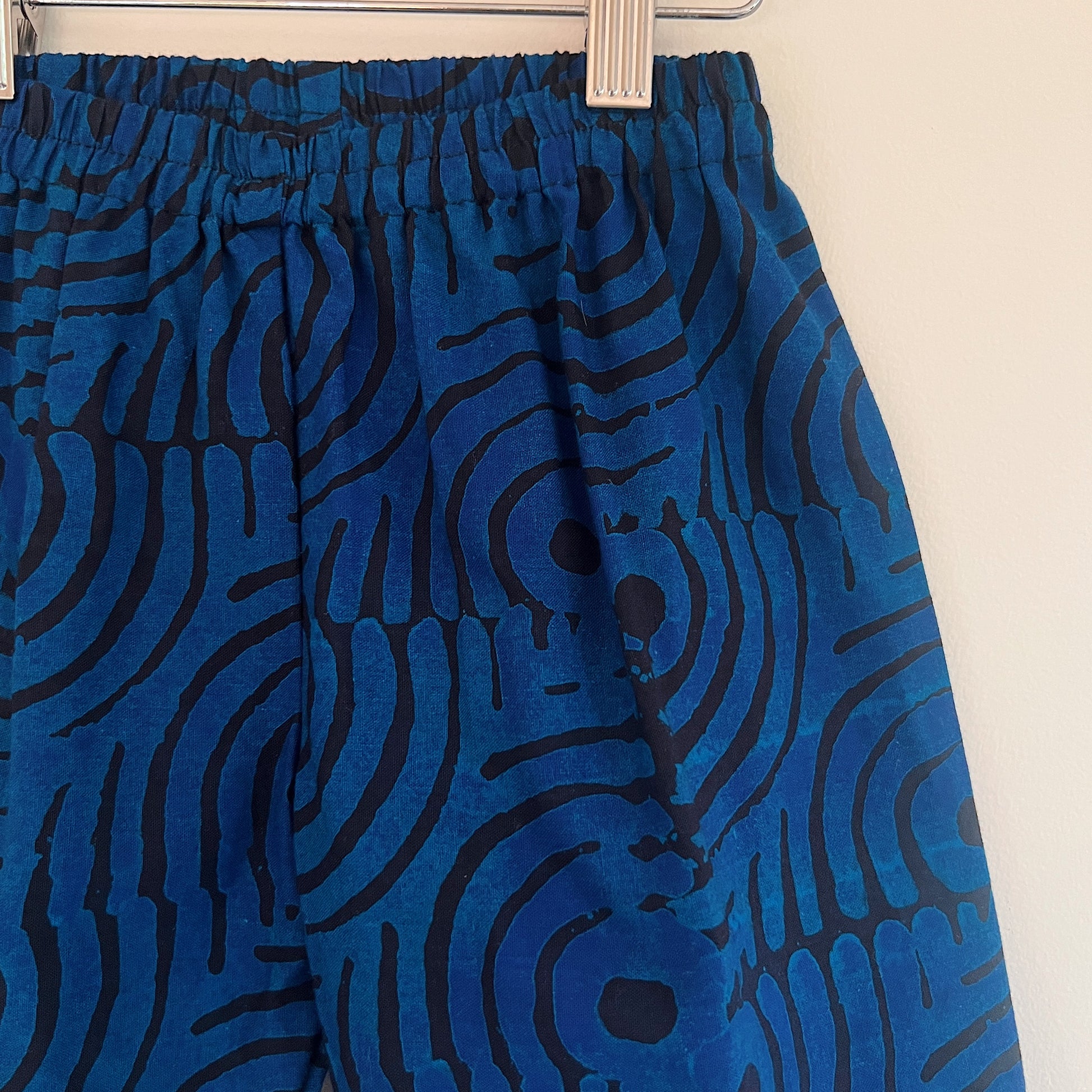 Close-up of the elasticated waistband and upper leg of the blue waves Batiki cotton kids pants, showing the hand-printed swirling wave and circle pattern in blue and navy