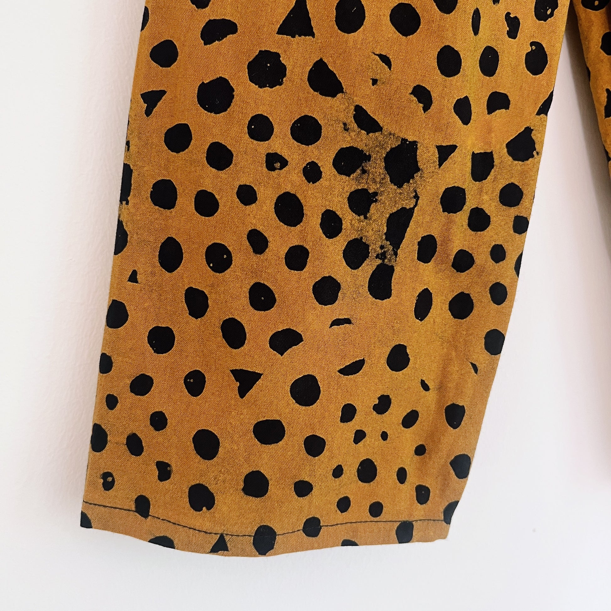 Close-up of the lower leg of the cheetah spot Batiki cotton kids pants, showing hand-printed black spots on golden amber cotton with natural hand-dye texture and hemline detail