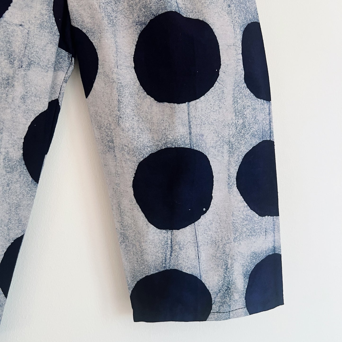 Close-up of the leg of the black dots Batiki cotton kids pants, showing large hand-printed black circles on a grey cotton ground with visible hand-dye texture and natural fabric variation