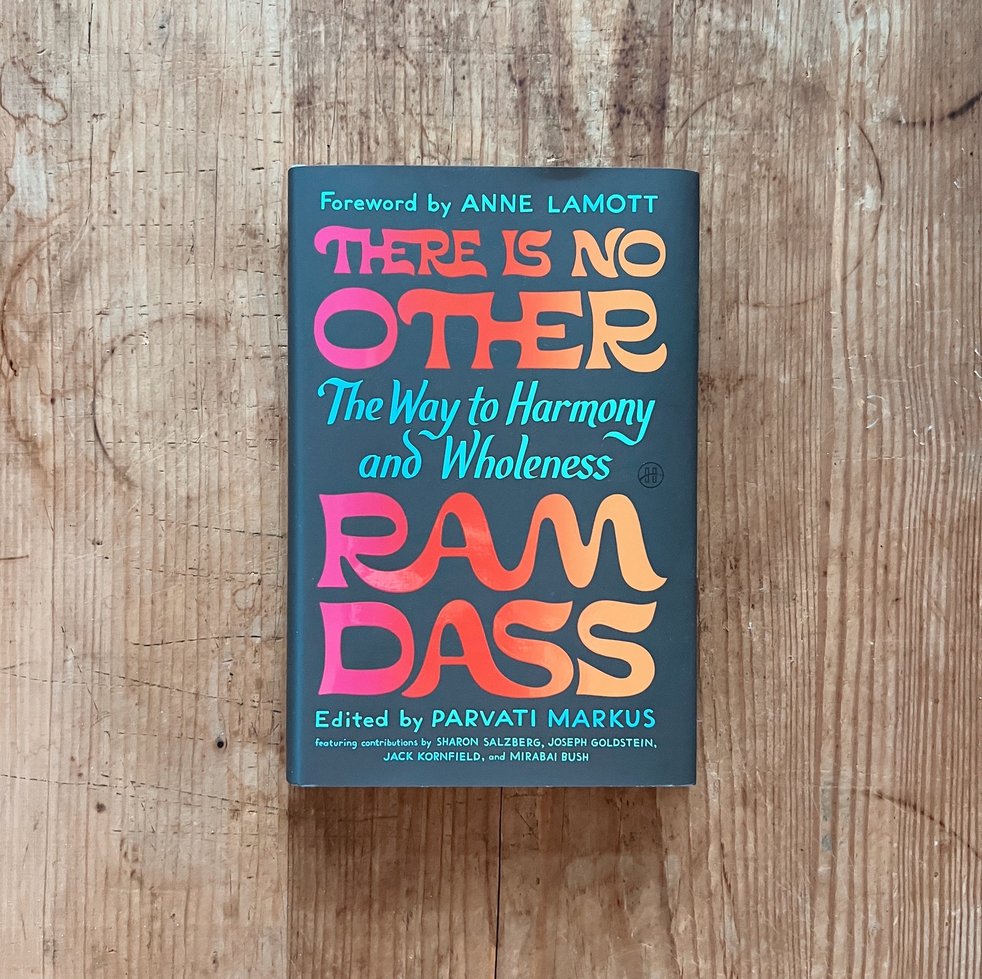Front cover of There Is No Other: The Way to Harmony and Wholeness by Ram Dass, displayed flat on a warm wood surface. The cover has a deep teal background with bold, retro-style display lettering in a warm gradient from hot pink to orange. The title "THERE IS NO OTHER" fills the upper half in large rounded block letters. Below in teal script: "The Way to Harmony and Wholeness." The author name "RAM DASS" appears in the same large gradient block lettering at the bottom. Above the title in small teal caps: "
