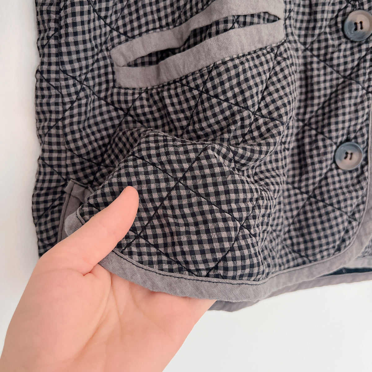 Cut Loose Easy Jacket in Iron Mini Check, close-up of a hand holding the gray-bound edge, showing the mini check fabric and diamond quilting.
