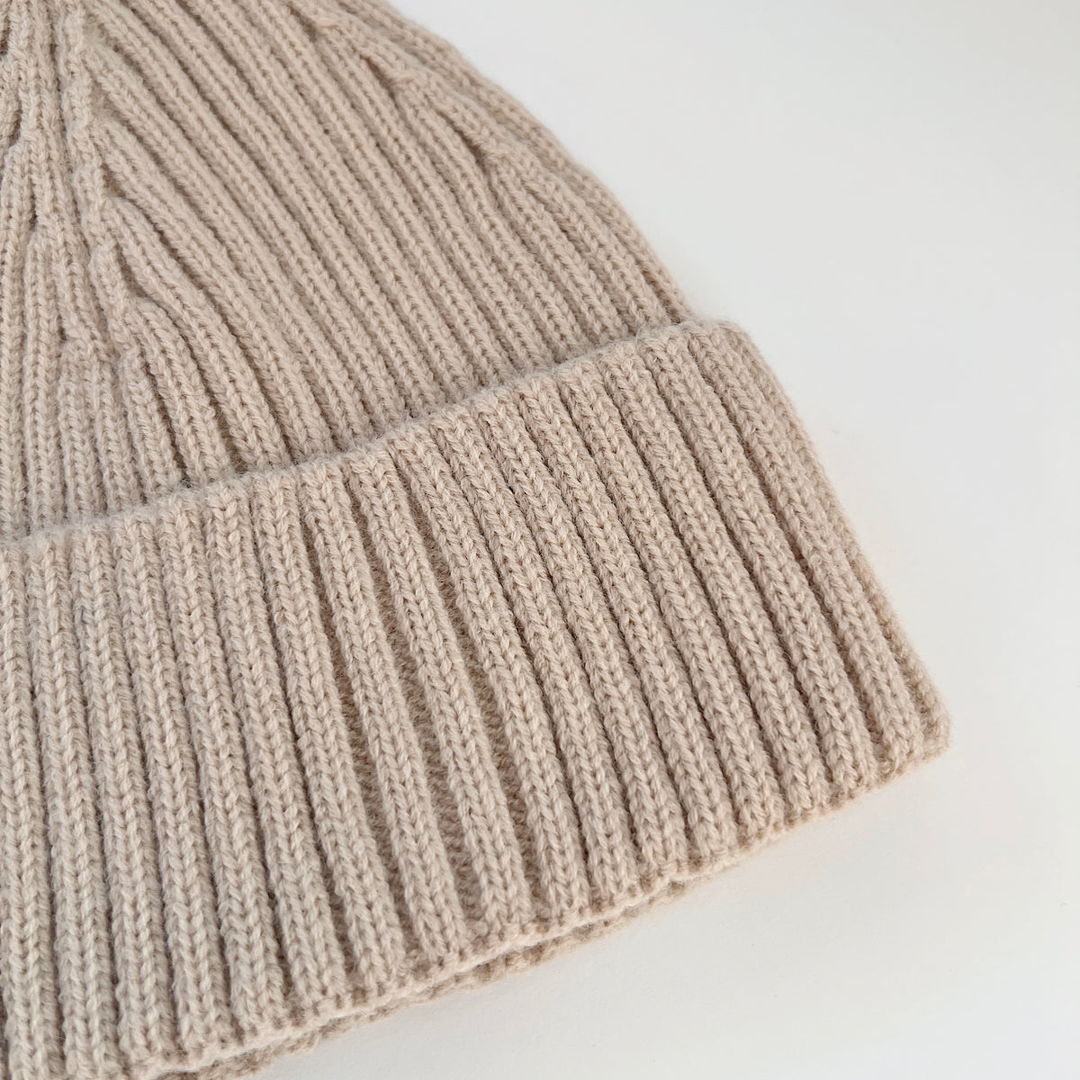 Close-up of the oatmeal lambswool beanie showing its ribbed knit texture and folded cuff.
