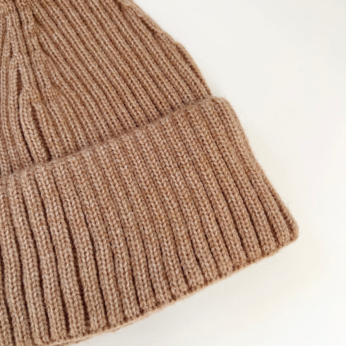 Close-up of the Toast brown lambswool beanie showing its ribbed knit texture and folded cuff.
