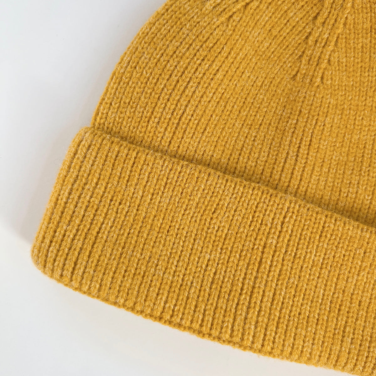 Close-up of the lemon yellow lambswool beanie showing its knit texture and ribbed folded cuff.
