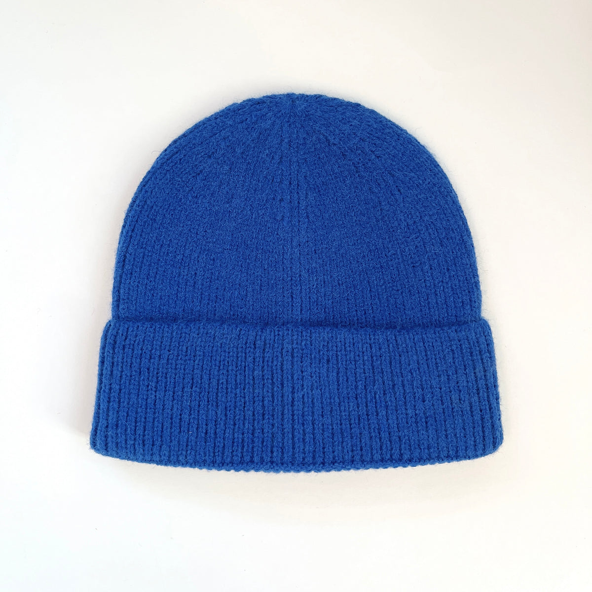 Ocean blue lambswool beanie laid flat with a rounded knit crown and ribbed fold-over cuff.
