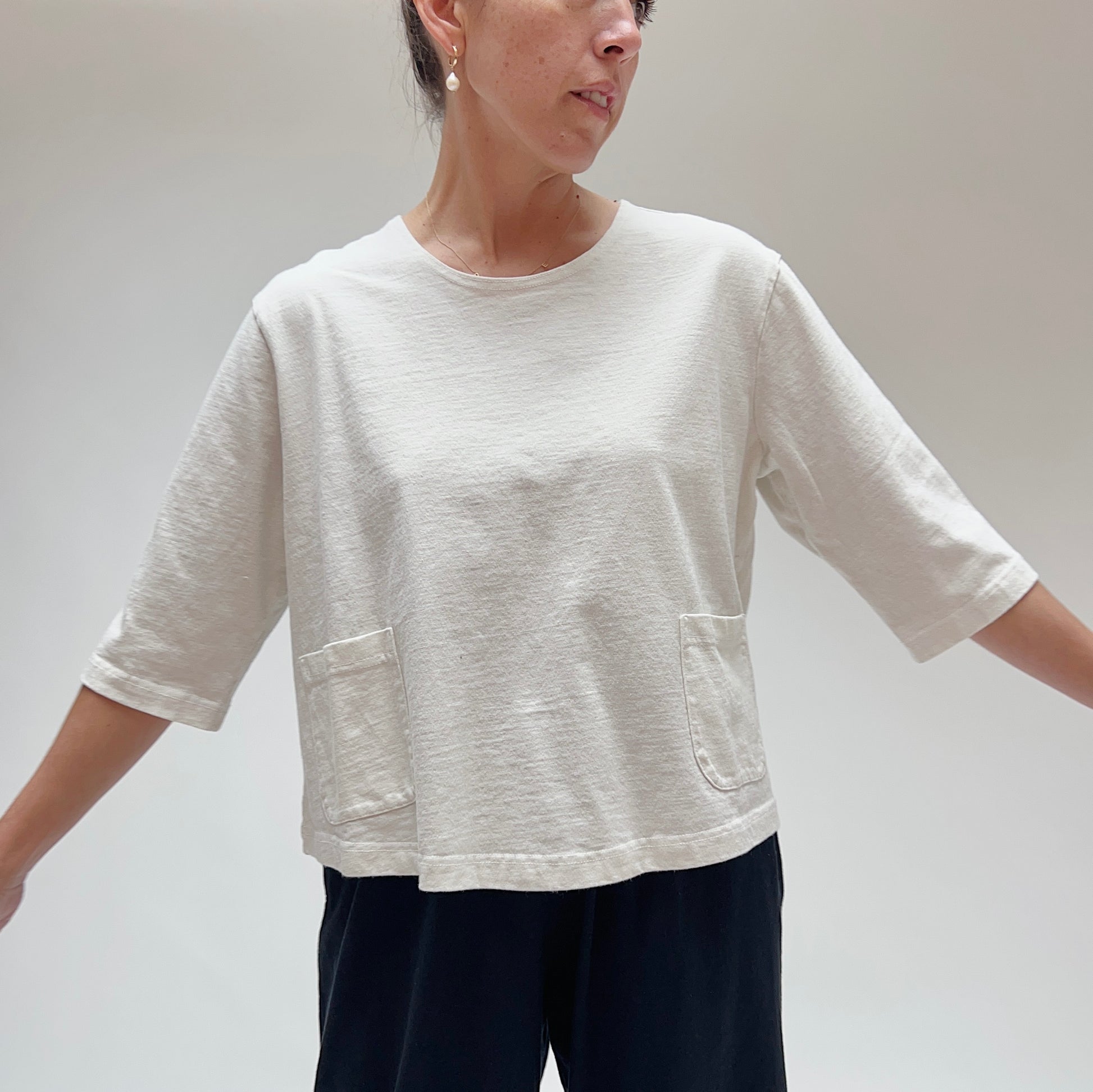 A person wearing a white, 3/4 sleeve cotton top with two front pockets, made by Pacific Cotton.