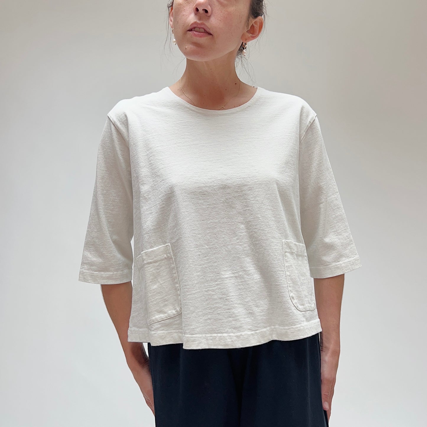 A person wearing a white, 3/4 sleeve cotton top with two front pockets, made by Pacific Cotton.