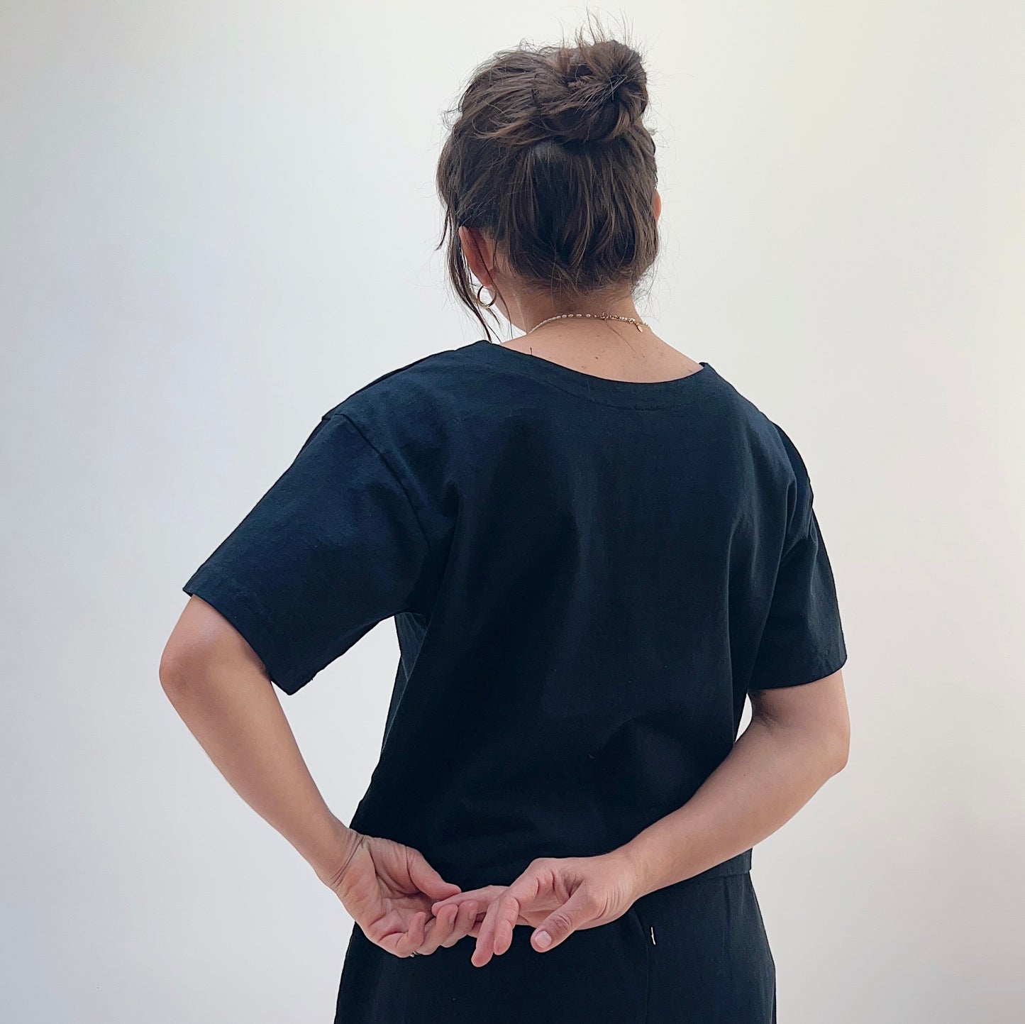 A person wearing a black crop V-neck t-shirt, viewed from the back